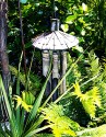 sun-bleached bamboo wind-chime hanging over green-gold ferns and slightly masked by the spikes of a green cordyline