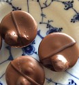 close up of three round milk chocloates each with a covered hazelnut and one darker chocolate stripe. They sit on a blue and white Copenhagen porcelain plate