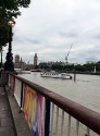 a view over the murky Thames, just down from the Festival Hall. Looking towards the Houses of Parliament. The early evening sky has a hint of pink, the lamps are lit and a banner attched to the railings proclaims 'love' in yellow, purple and pink colours.